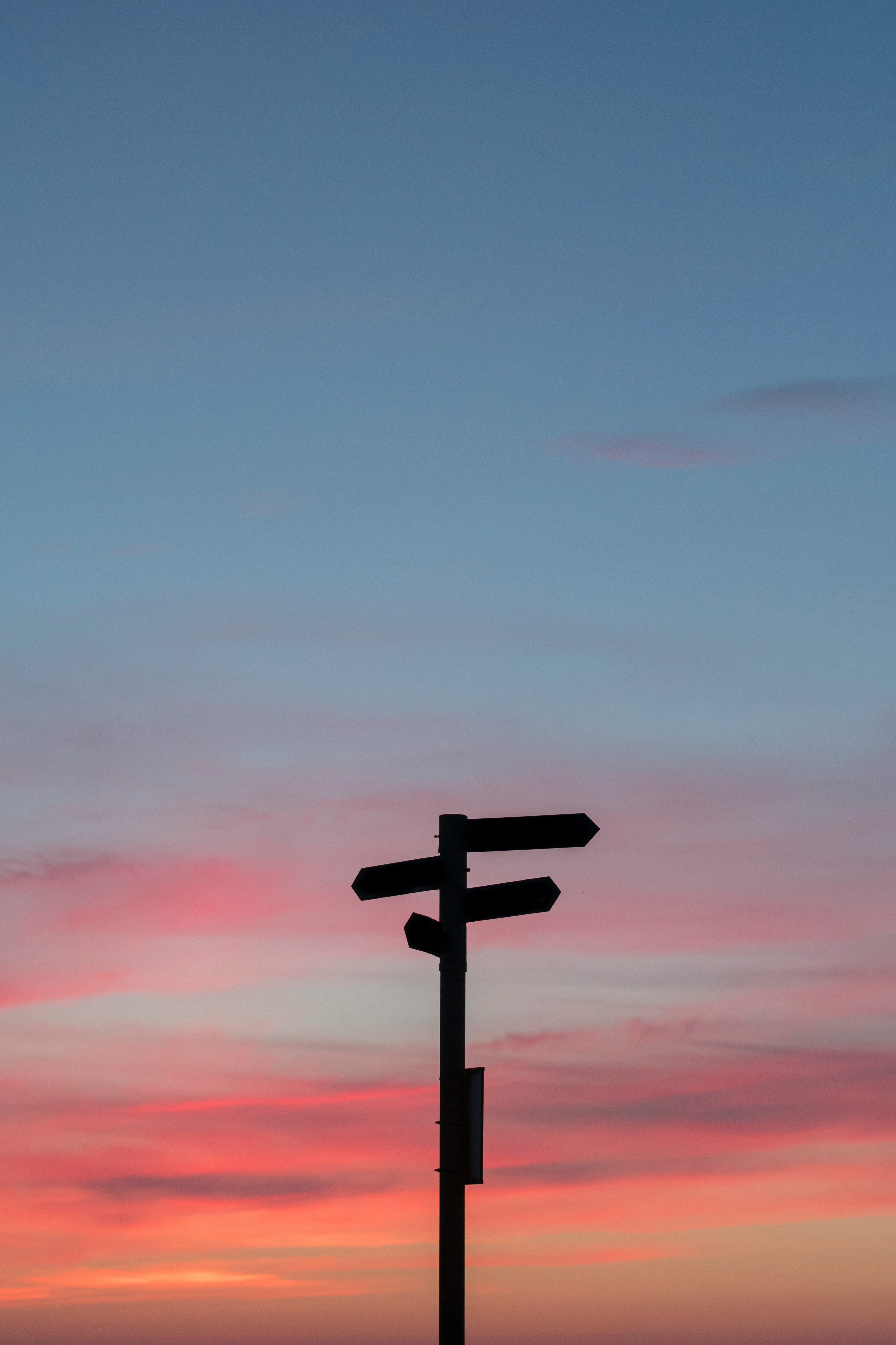 Multi-directional signpost silhouetted against a sunset sky